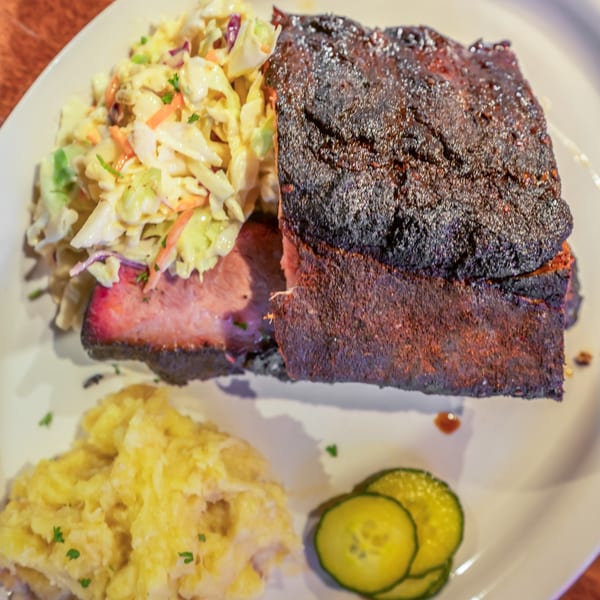 Flying Mango's southern-style BBQ brisket with coleslaw, mashed potatoes, and pickle slices.