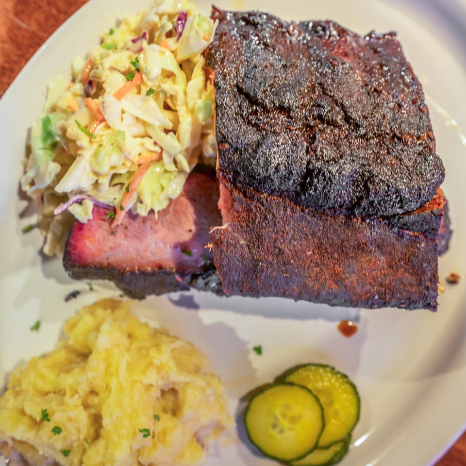 Flying Mango's southern-style BBQ brisket with coleslaw, mashed potatoes, and pickle slices.