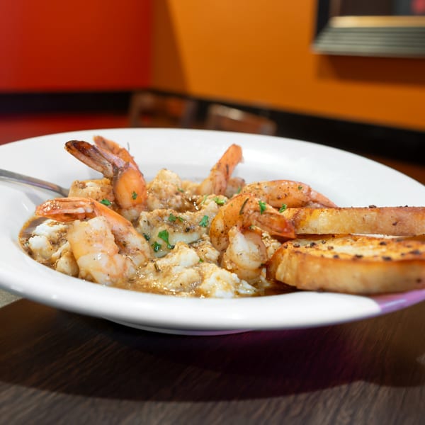 Shrimp and grits with toasted bread in a white bowl on a wooden table at Flying Mango.