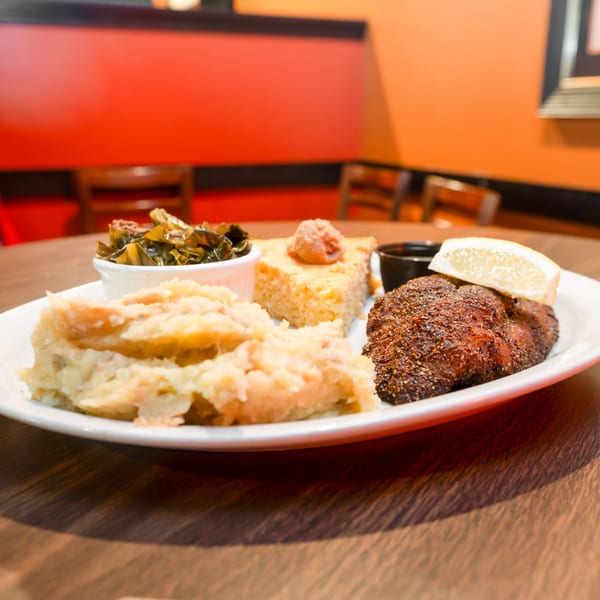 Southern meal with blackened fish, mashed potatoes, collard greens, and cornbread on a white plate.
