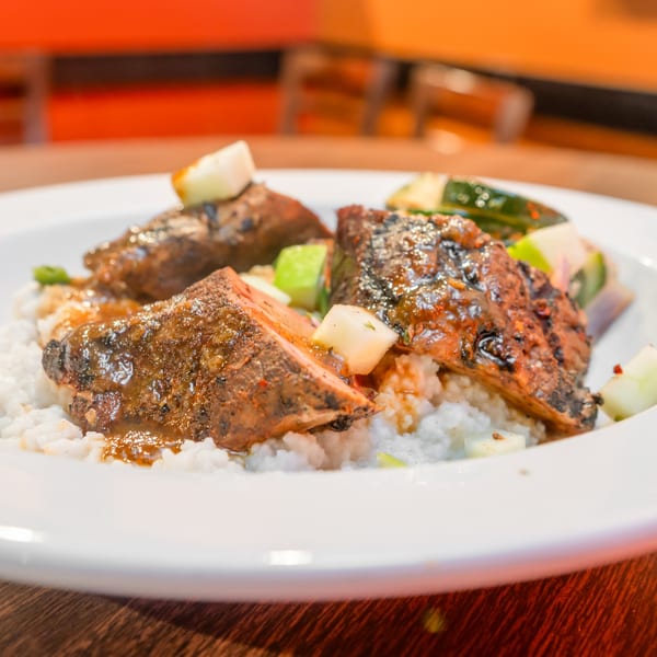 Close-up of Flying Mango's southern-style ribs with sauce, rice, and diced vegetables on a white plate.