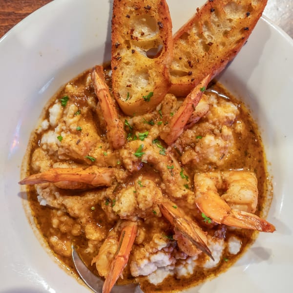 Shrimp and grits with a rich brown sauce, garnished with parsley and two pieces of toasted bread.