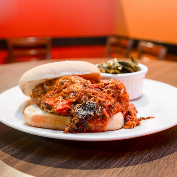 A Flying Mango pulled pork sandwich with a side of collard greens on a white plate.