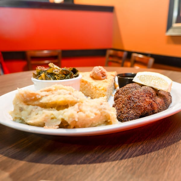 Southern-style meal with blackened fish, mashed potatoes, collard greens, and cornbread on a white plate.